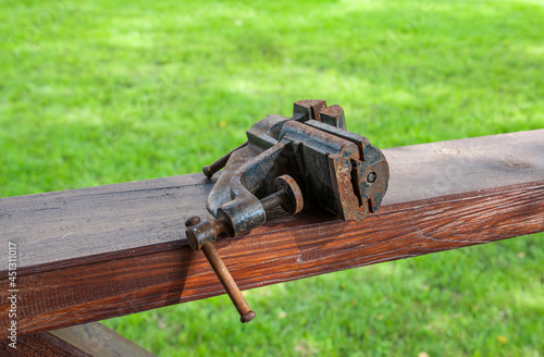 A rusty metal vise is lying on a wooden crossbar