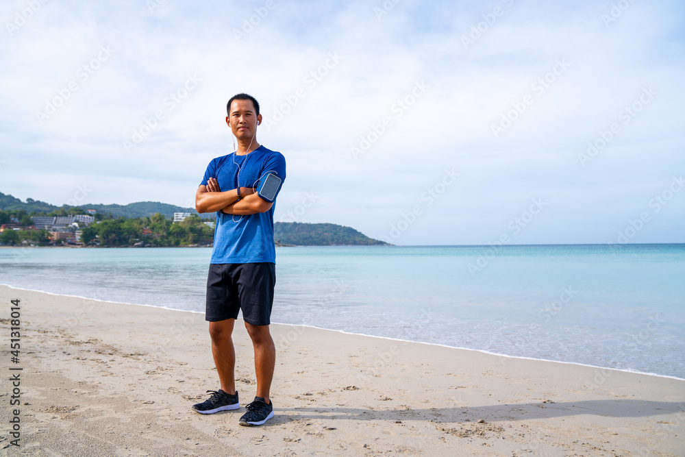 Healthy Asian man in sportswear jogging or running on the beach by the sea in summer morning. Strong athlete male do sport training workout fitness on the beach with listen to music from smartphone Healthy Asian man in sportswear jogging or running on the beach by the sea in summer morning. Strong athlete male do sport training workout fitness on the beach with listen to music from smartphone
