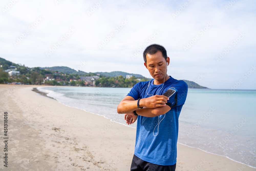 Healthy Asian man in sportswear jogging or running on the beach by the sea in summer morning. Strong athlete male do sport training workout fitness on the beach with listen to music from smartphone Healthy Asian man in sportswear jogging or running on the beach by the sea in summer morning. Strong athlete male do sport training workout fitness on the beach with listen to music from smartphone