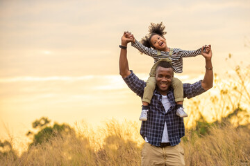 Happy mixed race family on holiday vacation. Smiling father and little daughter carrying and hiking together on meadow hill in summer. Parent with cute child girl relax and enjoy outdoors lifestyle.
