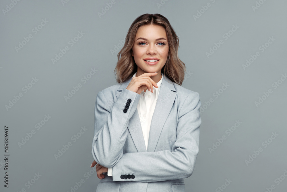 Successful young businesswoman touches chin with hand, smiling, looking at camera posing isolated on gray background. Studio portrait of successful friendly female lawyer in blazer and blouse Successful young businesswoman touches chin with hand, smiling, looking at camera posing isolated on gray background. Studio portrait of successful friendly female lawyer in blazer and blouse