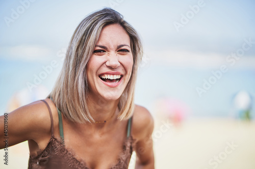 Young cheerful woman standing and laughing on the beach © Daniel