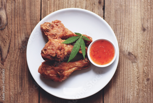 Crispy fried chicken food with cannabis leaf - marijuana leaves plant, Cannabis food nature herb concept, Fried chicken leg on plate with chicken dipping sauce