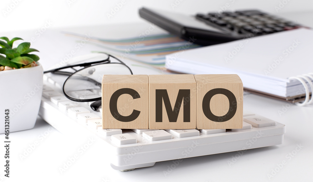 Fototapeta premium CMO Chief Marketing Officer written on a wooden cube on keyboard with office tools