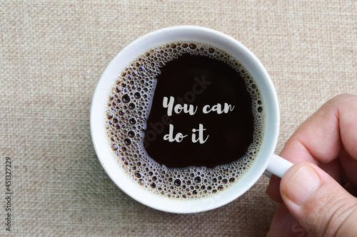 Hand holding a cup of coffee with text YOU CAN DO IT.