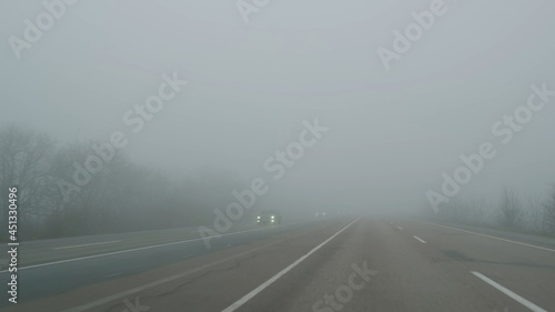 Cars move on foggy road, view through windshield in daytime. Cars pass through fog on road. Poor visibility in mist highway. Dangerous weather for driving. Cars keep distance at haze