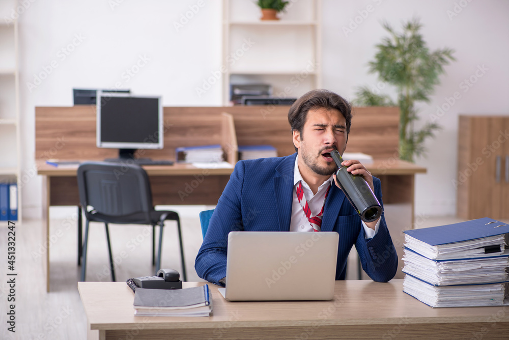 Young alcohol addicted male employee working in the office Young alcohol addicted male employee working in the office