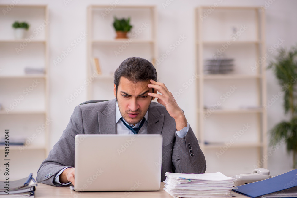 Young male employee unhappy with excessive work in the office Young male employee unhappy with excessive work in the office