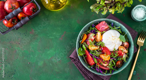 Salad with tomatoes, arugula, Burrata cheese and microgreens on a green stone background, top view. copy space