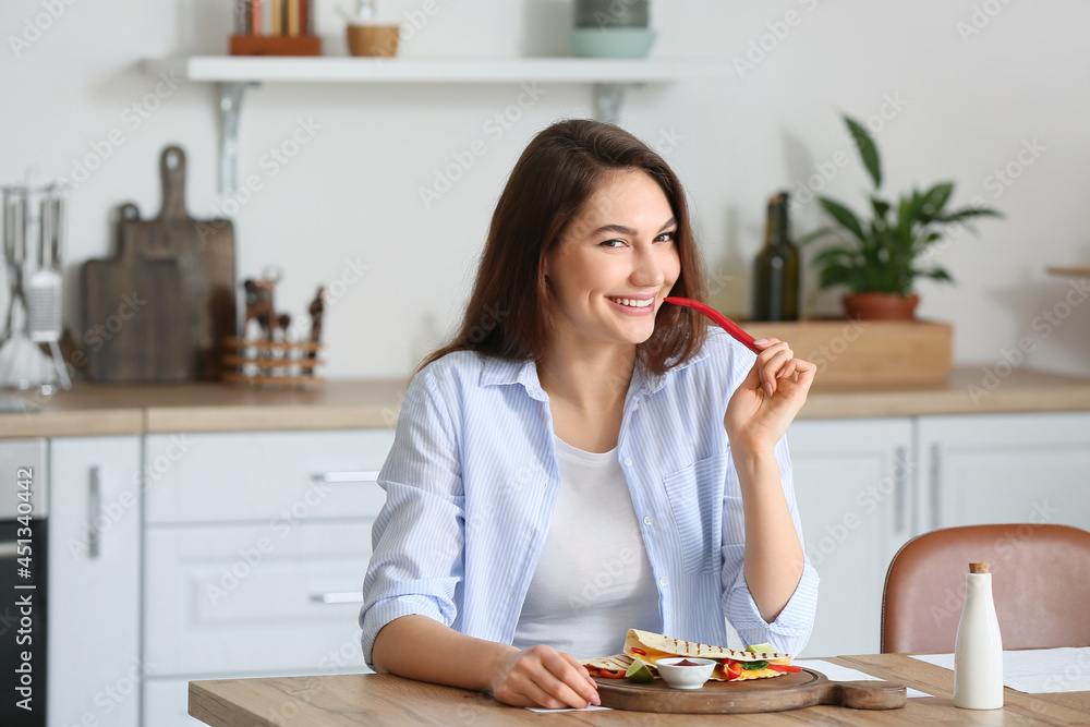 Beautiful young woman eating tasty quesadilla at home