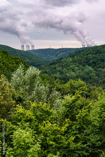 Green valley covered with forest and on the horizon are the cooling towers of a nuclear power plant Dukovany. Contrast of nature and industry. Czech republic.