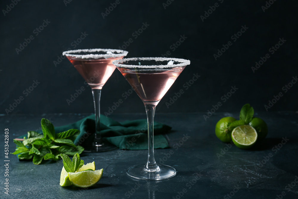Glasses of tasty cosmopolitan cocktail, mint and limes on dark background