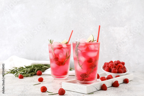 Glasses of tasty raspberry lemonade and berries on light background