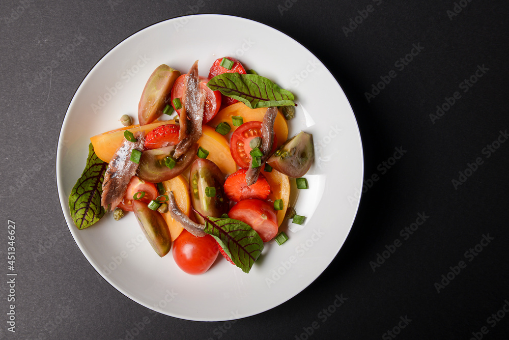 Vegetable salad made of tomatoes and fish slices, served in a white plate over black background. Vegetable salad made of tomatoes and fish slices, served in a white plate over black background.