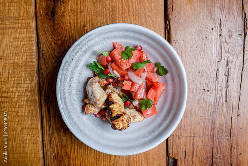 Meat with tomato and pomegranate seeds salad served in a bowl over rustic wooden background.