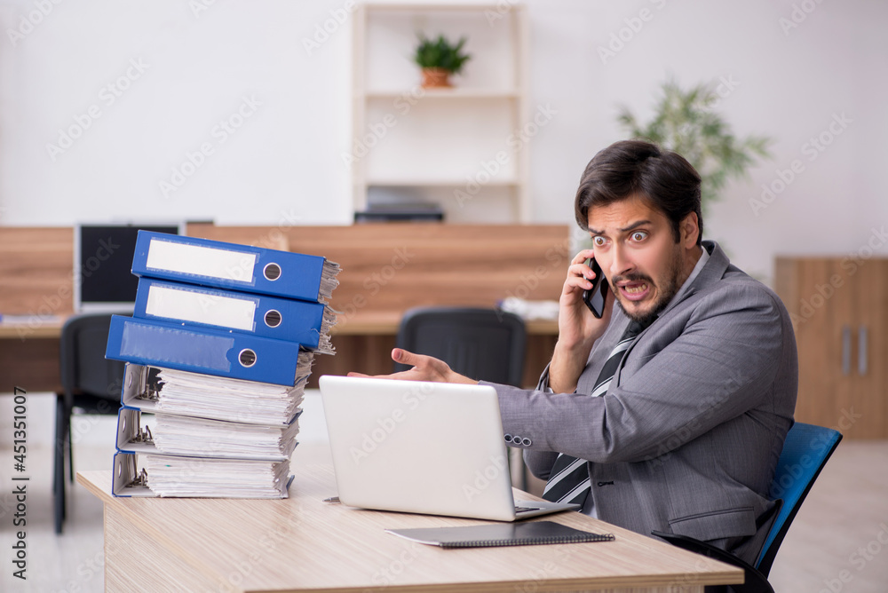 Young male employee unhappy with excessive work in the office Young male employee unhappy with excessive work in the office