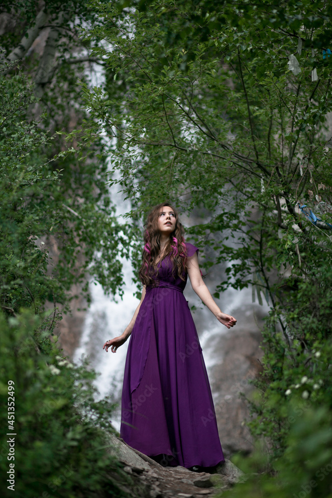 girl in a purple dress against the background of a mountain waterfall
