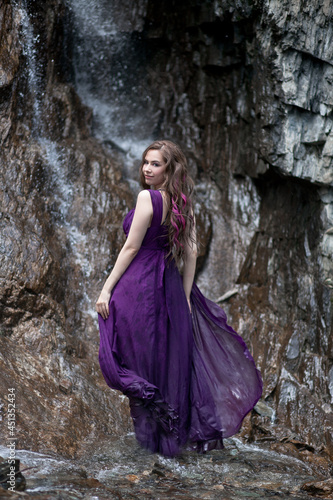 girl in a purple dress against the background of a mountain waterfall