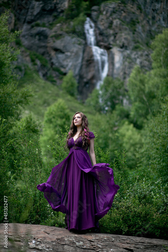 girl in a purple dress against the background of a mountain waterfall