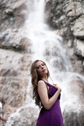 girl in a purple dress against the background of a mountain waterfall © AKaltykova