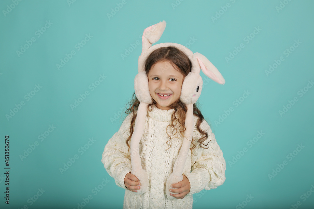 a beautiful happy brown-haired girl with curly hair in a white sweater with pink bunny ears on a blue background