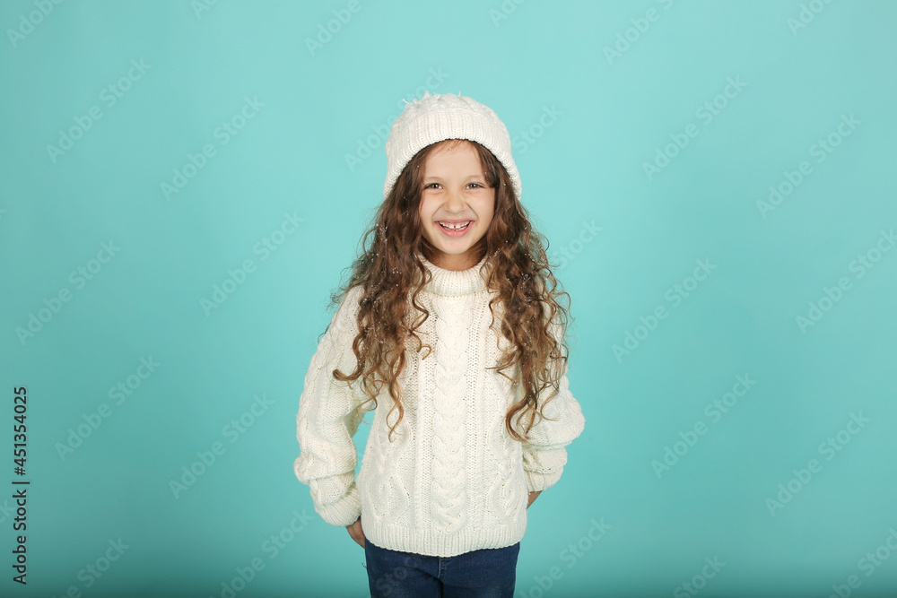 beautiful happy brown-haired girl with curly hair white sweater and winter hat blue background with snow in her hair beautiful happy brown-haired girl with curly hair white sweater and winter hat blue background with snow in her hair