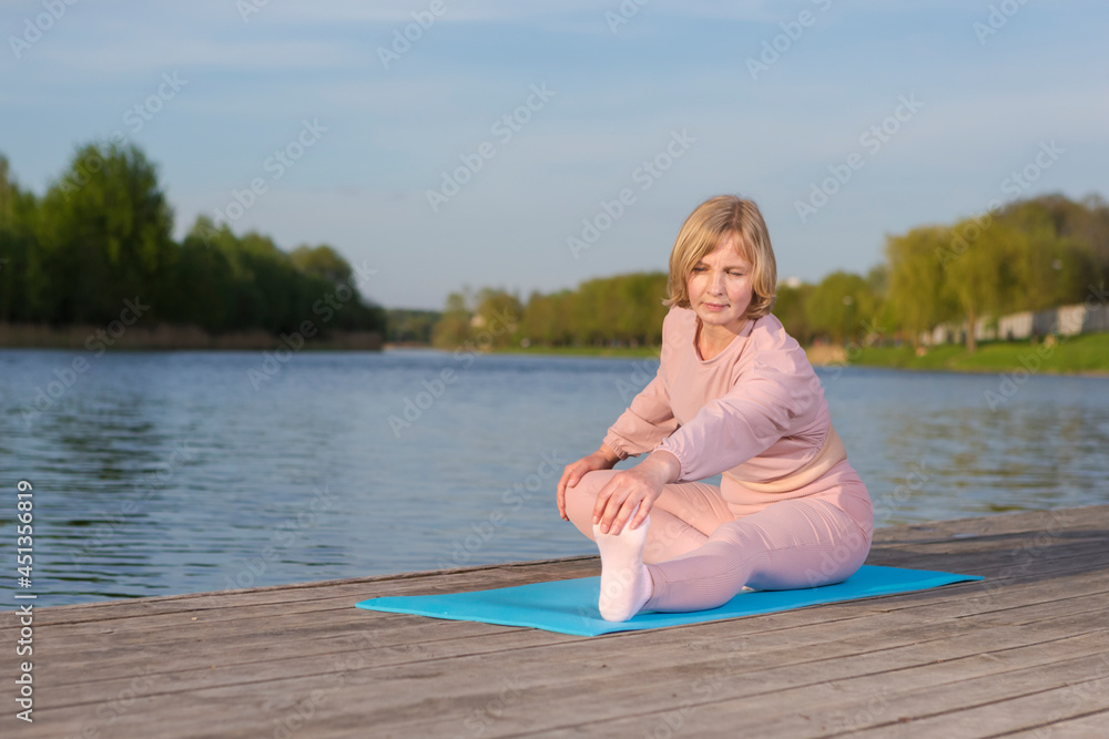 Sport Ideas. Mature Caucasian Woman During Yoga Legs Stretching Training On Wooden Stage Near Water Outdoor.