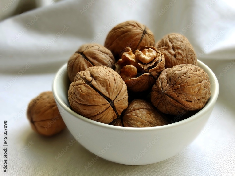 Walnuts in a white bowl on a white linen cloth, one nut is cracked open Walnuts in a white bowl on a white linen cloth, one nut is cracked open