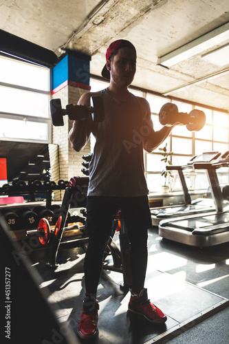 Silhouette photo of a man performing exercises with dumbbells in the gym.