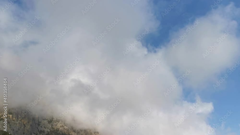 Clouds mountains view from below. Huge fluffy clouds float below the tops of the mountains. Slow atmospheric movement. Natural textured background . The blue sky is covered with large cotton clouds Clouds mountains view from below. Huge fluffy clouds float below the tops of the mountains. Slow atmospheric movement. Natural textured background . The blue sky is covered with large cotton clouds