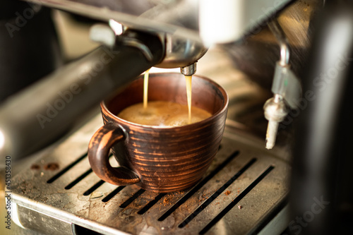 Coffee is prepared in a coffee machine. Freshly made coffee is poured into an earthenware cup.