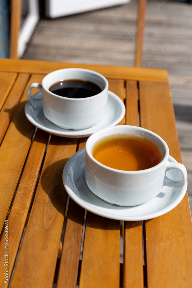 a cup of coffee and a cup of tea on a wooden table on the veranda of the house on a sunny morning