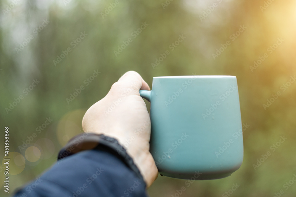 Cup in a man's hand against a background of green forest. Cup in a man's hand against a background of green forest.