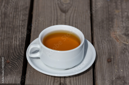 a cup of tea in a white mug and saucer on a wooden background on a sunny morning outside