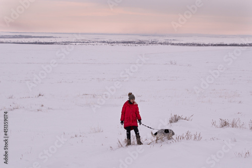 A girl in a red jacket with a dog in a snow field..The concept of winter.