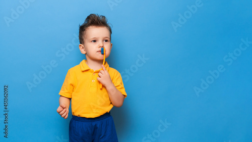 Happy child kid boy brushing teeth with toothbrush on blue background. Health care, dental hygiene. Mockup, copy space