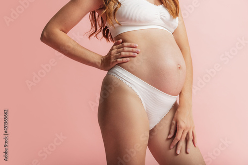 Close up young beautiful pregnant woman's body, belly isolated over pink color studio background. Natural beauty, happy motherhood, femininity concept.