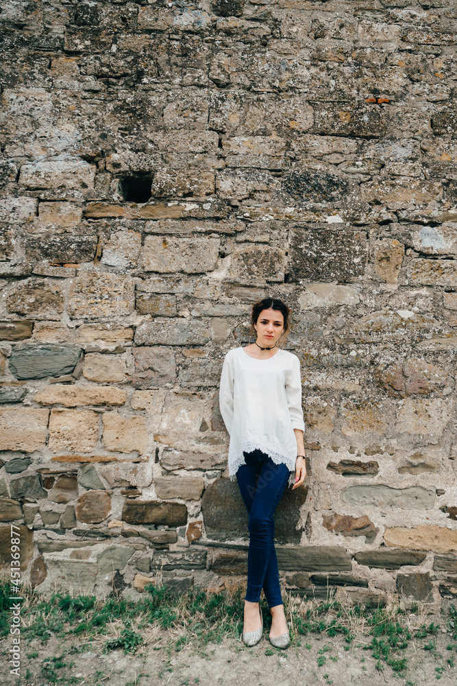 portrait of traveler girl in white dress stands at ancient stone wall