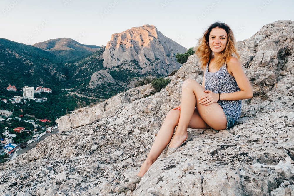 happy young sexy girl traveler is sitting on the top of a mountain