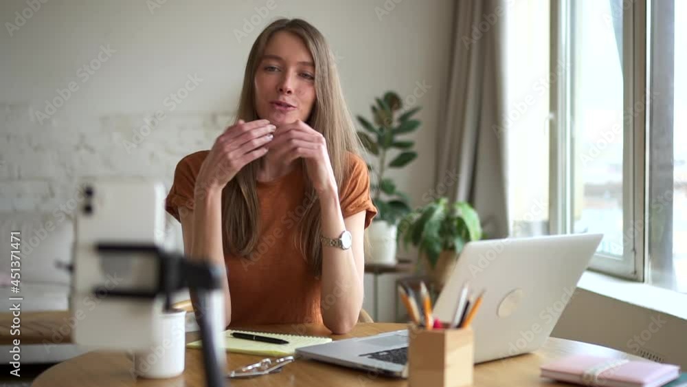 Woman having online talk in front of smartphone screen and sitting at table in home room. Woman having online talk in front of smartphone screen and sitting at table in home room.
