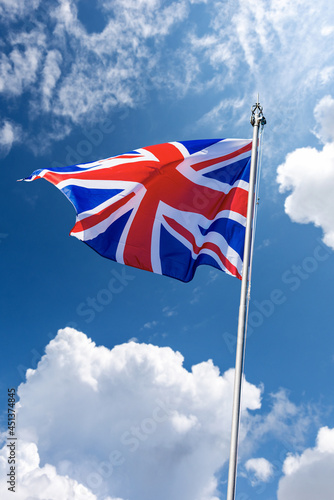 Union Jack Flag. Close-up of a national UK flag with flagpole, blowing in the wind on a blue sky with clouds and copy space.