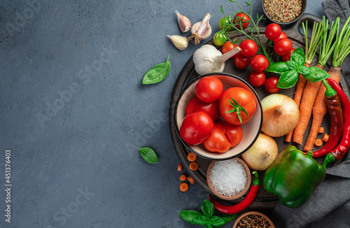 Fresh vegetables, spices, ingredients for making tomato sauce on a gray-blue background.