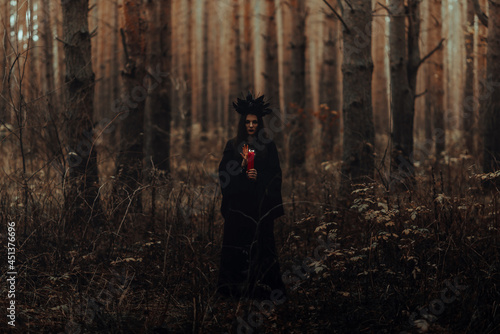 witch in a black costume performs dark spells with candles