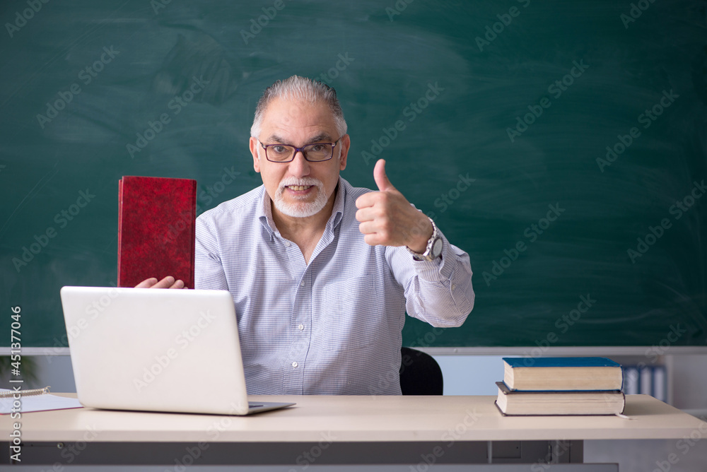 Old male teacher in front of green board