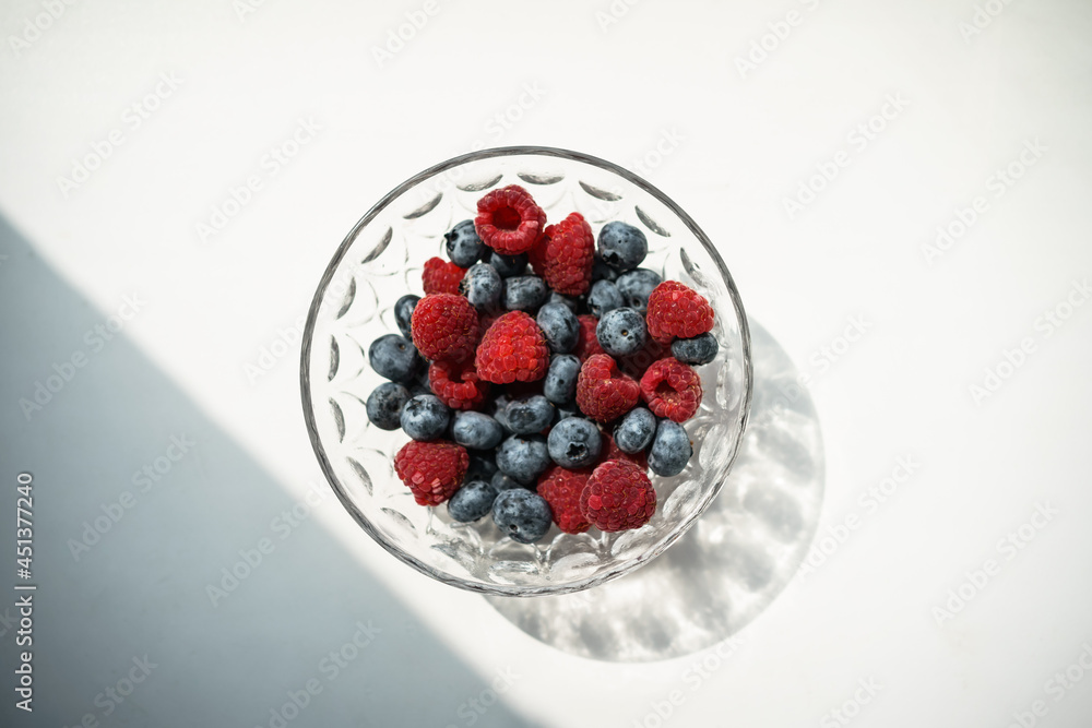 raspberries and blueberries in a transparent bowl on a white background raspberries and blueberries in a transparent bowl on a white background