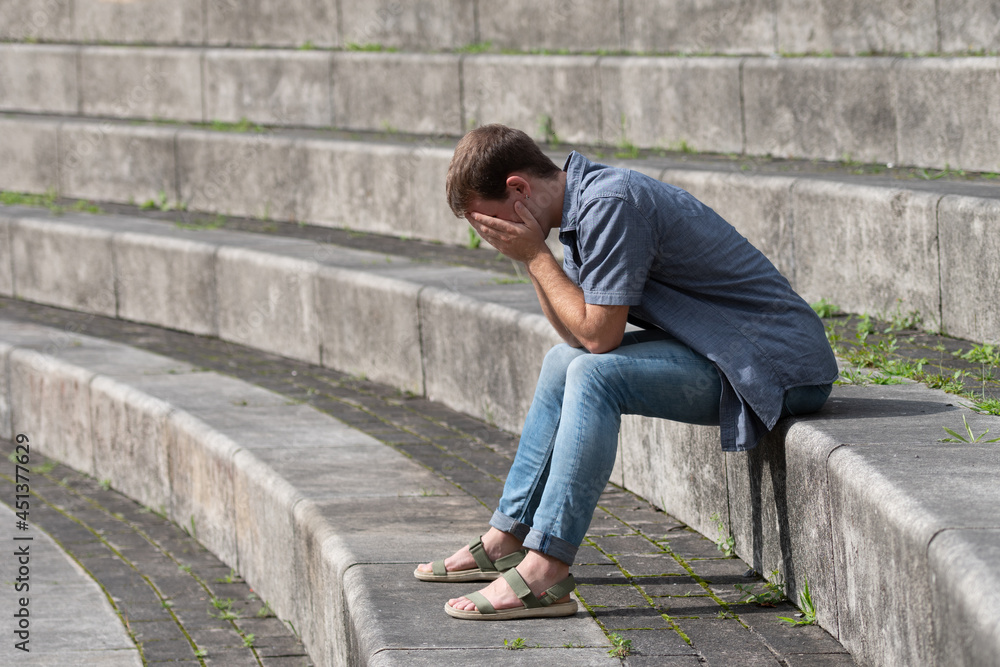 Young man with depression sitting on grandstand steps while covering his face and crying