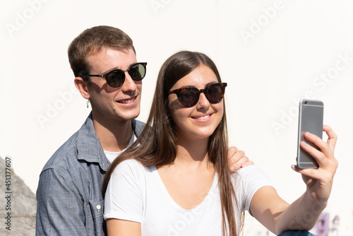 Young couple taking a selfie with a smartphone outdoors in a sunny day
