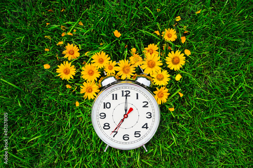 Postcard good morning and alarm clock with yellow flowers lie on the green grass
