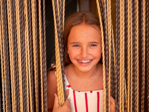 Portrait of a young caucasian girl with braces smiling through the curtains