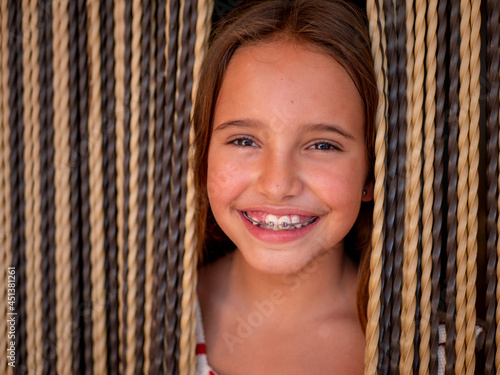Portrait of a young caucasian girl with braces smiling through the curtains